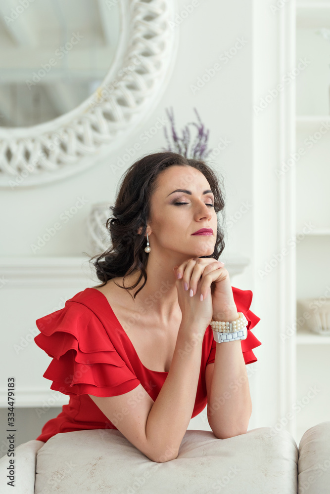 portrait of a young attractive brunette woman in pensive prayer leaned on the back of a chair in a red dress portrait of a young attractive brunette woman in pensive prayer leaned on the back of a chair in a red dress