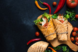 Mexican corn tortilla wrap with grilled chicken and fresh vegetables served on a wooden cutting board. Dietary healthy dish. Black background, flat lay, copy space