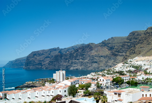 A panoramic view of a bay at the seaside resort of Los Gigantes on the holiday island of Tenerife. Steep volcanic cliffs make a dramatic background. A beautiful scene with a clear blue sky. 