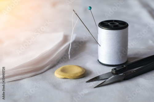 Needle and pin on white thread rolls for hand sewing on white cloth with tape measure and sketch yellow chalk with scissors cut on the fabric orange light close-up.