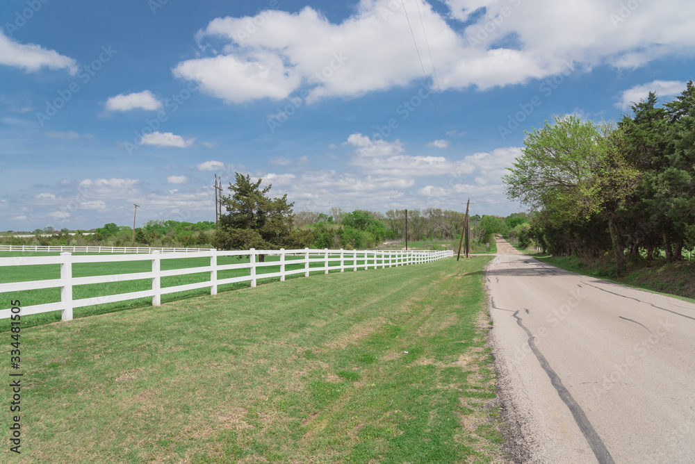 Scenic country road along long white fence leads to horizontal in cloud blue sky in Ennis, Texas, USA