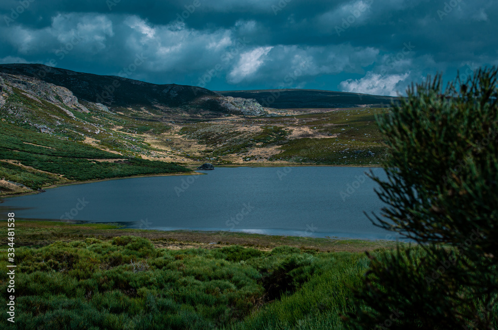 paisaje con lago rodeado de monte verde y una tormenta