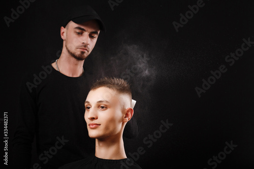 Hairdresser in black cap sprays water on client's hair. Hairdressing process in the barber shop.