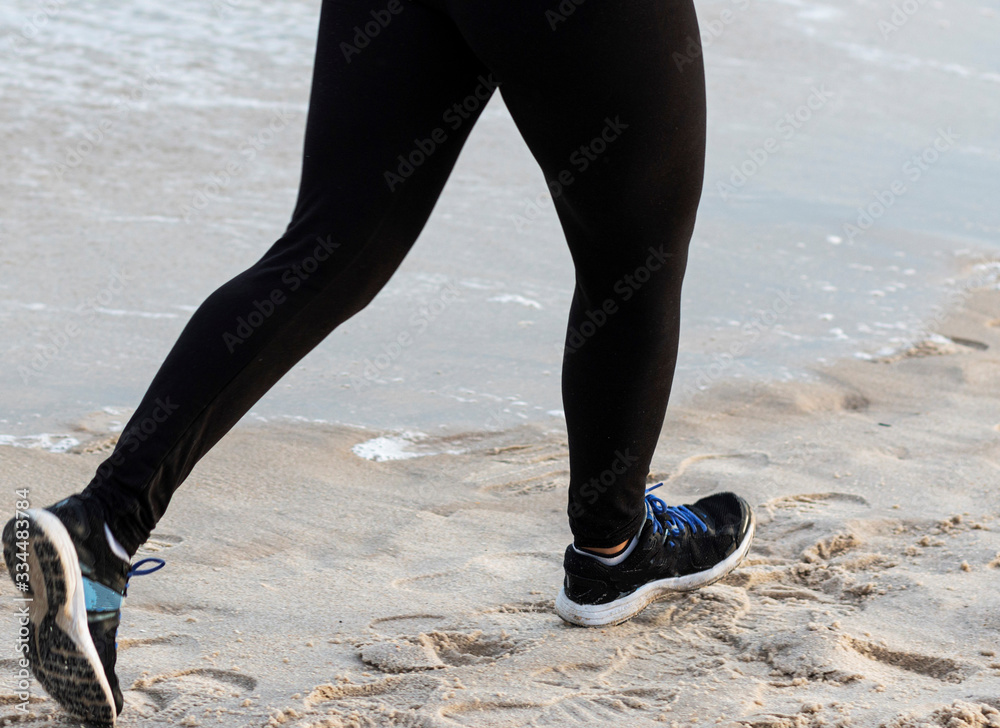Runners legs in black spandex on the sand at the beach next to the water Runners legs in black spandex on the sand at the beach next to the water
