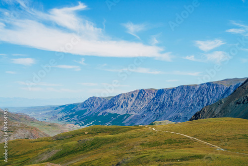 Beautiful aerial view to green hill and great mountains under blue sky. Long mountain range and long valley with forest. Awesome alpine landscape in sunny day. Vivid highland scenery on high altitude.