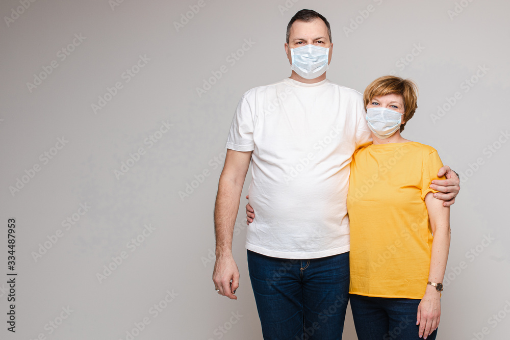 Beautiful caucasian man wears white t-shirt stands with cheerful caucasian woman wears yellow t-shirt in white medical masks and hugs together Beautiful caucasian man wears white t-shirt stands with cheerful caucasian woman wears yellow t-shirt in white medical masks and hugs together