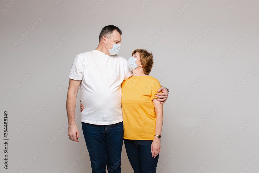 Adult husband and wife in protective masks looking at each other isolated on grey background. Infection and quarantine concept Adult husband and wife in protective masks looking at each other isolated on grey background. Infection and quarantine concept