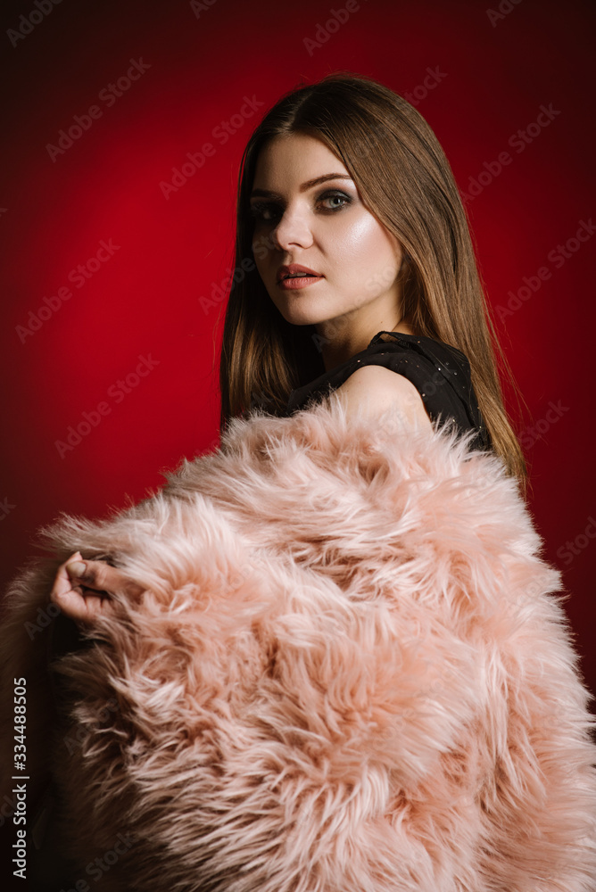 Fashion portrait of woman wearing a fur on black and red background