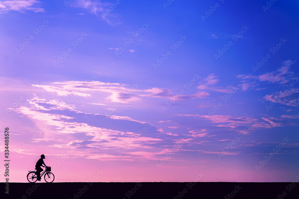 Silhouette of a cyclist against the pink dawn sky on the beach in Bali. A man on a Bicycle rides alone against a pink and blue sky.