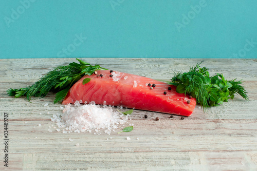 Sliced piece of salmon, a handful of pink coarse salt and greens on the table photo