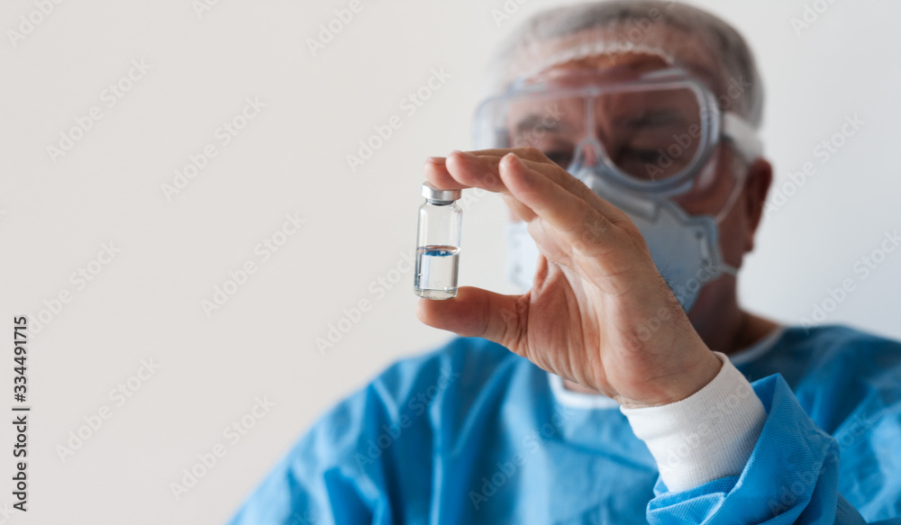 Coronavirus Covid-19 concept. Doctor in glasses and a respirator mask for protection holds a vaccine bottle. Wuhan, China epidemic virus Cov-19 symptoms quarantine background Corona virus outbreaking. Coronavirus Covid-19 concept. Doctor in glasses and a respirator mask for protection holds a vaccine bottle. Wuhan, China epidemic virus Cov-19 symptoms quarantine background Corona virus outbreaking.