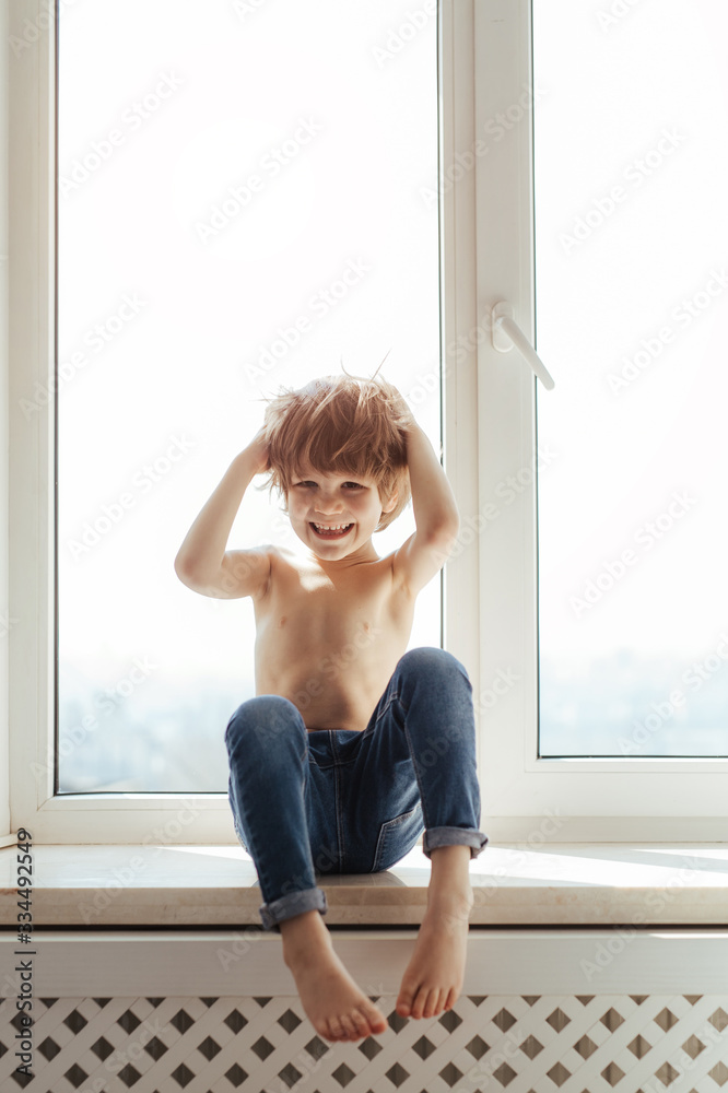Topless kid portrait near the window. Sunny day outside. Bright white room. Boy poses, smiles and having fun alone. Topless kid portrait near the window. Sunny day outside. Bright white room. Boy poses, smiles and having fun alone.