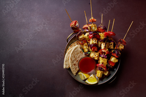 Paneer tikka starter kebabs with mint chutney and chapati. Traditional indian cuisine, grilled cheese skewers with onion and bell pepper slices. Vegetarian dish marinated in tikka sauce.