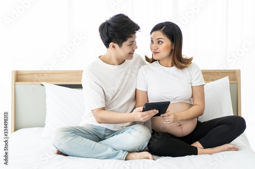 Romantic husband and wife using tablet on the bed in bedroom to brows and search an information on the internet. Leisure activity in  holiday for pregnant woman and husband. Together activity
