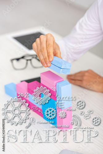 Cropped view of businesswoman making marketing pyramid from colorful building blocks on table, startup illustration