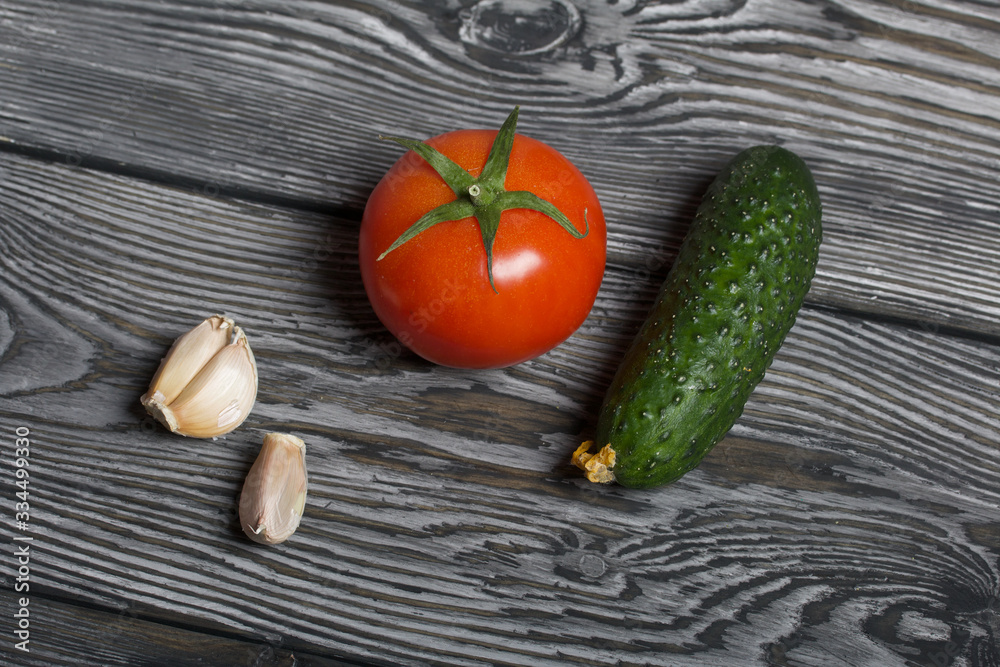 Tomato with a green ponytail, cucumber and garlic. They lie on the surface of brushed pine boards. Tomato with a green ponytail, cucumber and garlic. They lie on the surface of brushed pine boards.