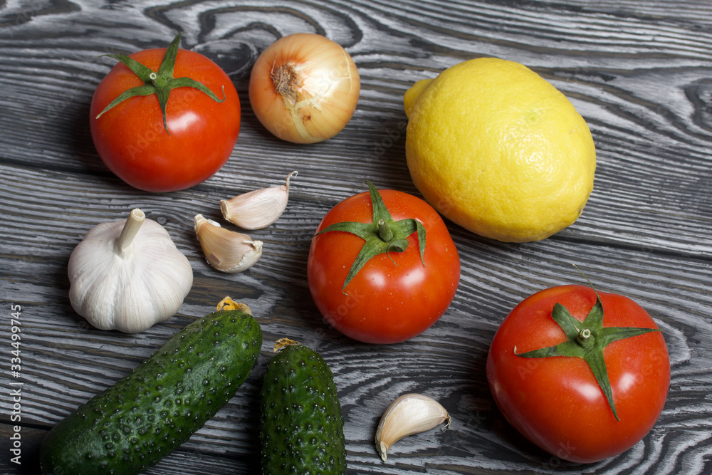 Tomatoes with green ponytails, onion, lemon and garlic head. Two green prickly cucumbers with yellow flowers. They lie on the surface of brushed pine boards. Tomatoes with green ponytails, onion, lemon and garlic head. Two green prickly cucumbers with yellow flowers. They lie on the surface of brushed pine boards.