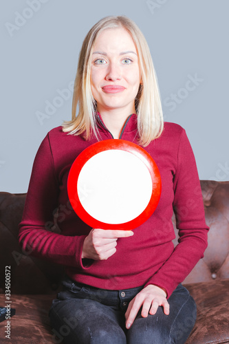 Mockup image of young woman sitting on the couch holding a warning sign