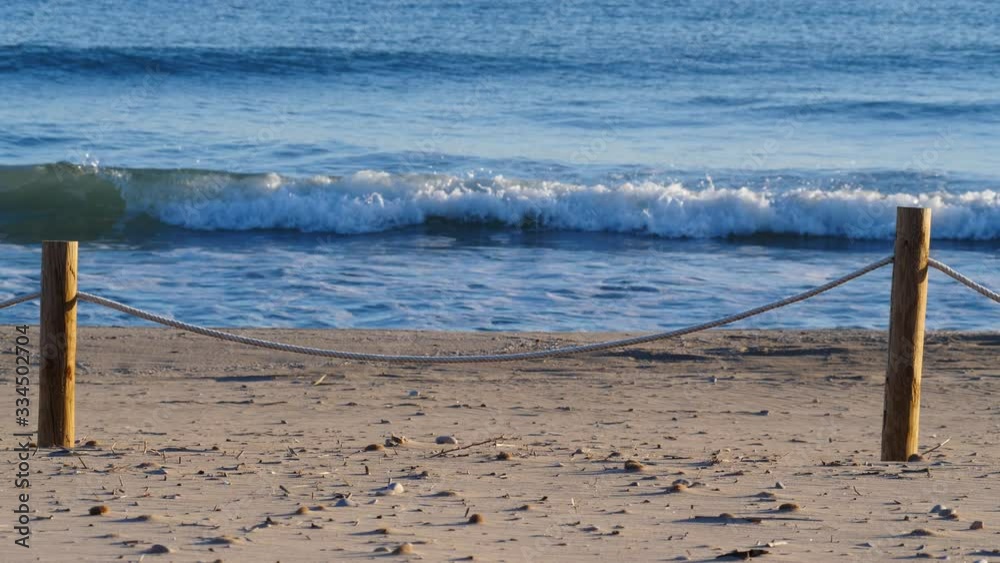 Rope boundary fences protecting dune system on beach. Sandy sea shore with waves splashing in slow motion Rope boundary fences protecting dune system on beach. Sandy sea shore with waves splashing in slow motion