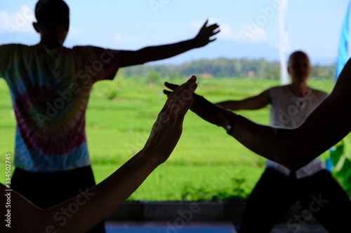 Hands of people in the shade engaged in the practice of qigong energy with a direction teacher in the background.  © KrutSolt