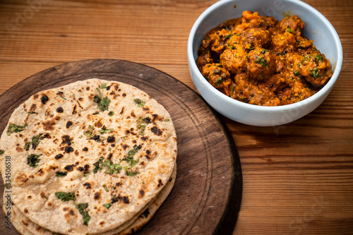 Potato curry (Kashmiri dum aloo) with chapatti (roti) served on wooden dining table.