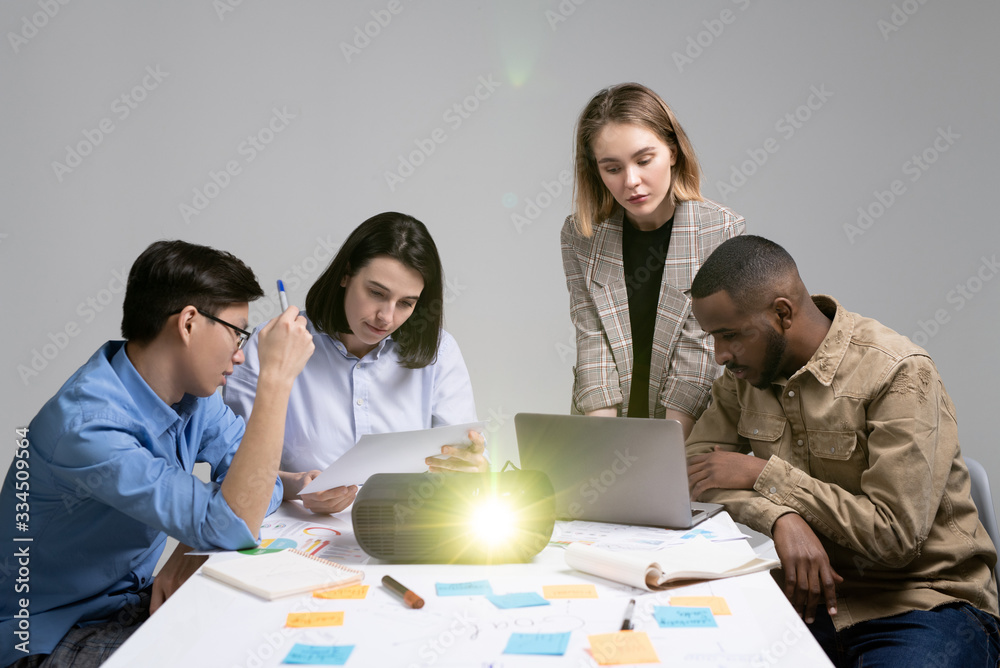 Group of thoughtful young multi-ethnic managers focused on tasks analyzing information using laptop and report data Group of thoughtful young multi-ethnic managers focused on tasks analyzing information using laptop and report data