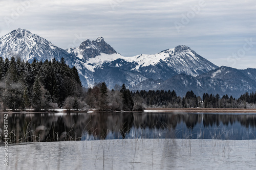 Landscape of a specular reflection in the lake, a dry grass, a cane and snags in the foreground, mountains and the forest on a background, ice on water, grass is covered with hoarfrost, tranquillity