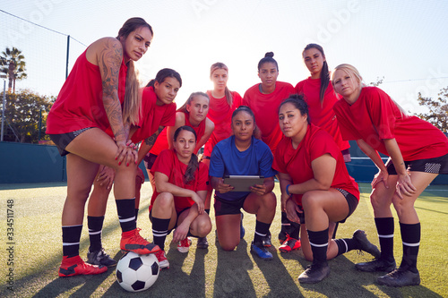 Portrait Of Coach Holding Digital Tablet With Womens Football Team Training For Soccer Match 