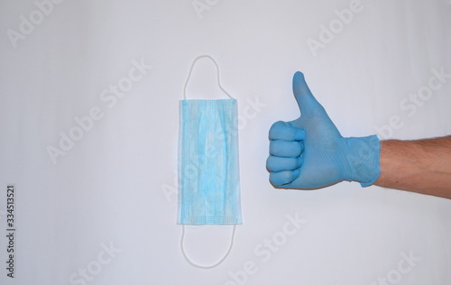 hand in blue glove with thumb up and mask