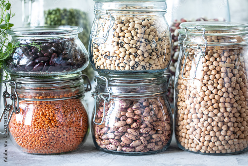 Set of different legumes in glass jars on, concrete white table. A source of protein for vegetarians. The concept of healthy eating and food storage. Set of different legumes in glass jars on, concrete white table. A source of protein for vegetarians. The concept of healthy eating and food storage.