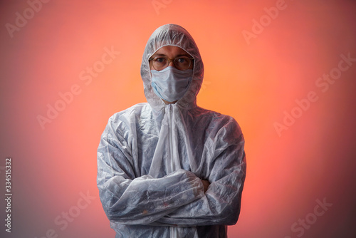 Man doctor in protective suit, medical mask, goggles with arms crossed on red background. Coronavirus covid-19 concept