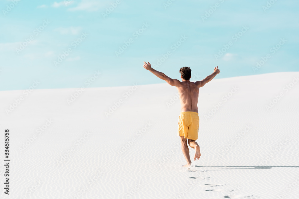 back view of man in swim shorts with muscular torso running on sandy beach back view of man in swim shorts with muscular torso running on sandy beach