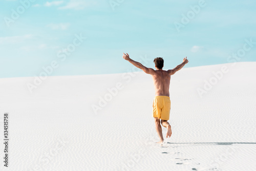 back view of man in swim shorts with muscular torso running on sandy beach