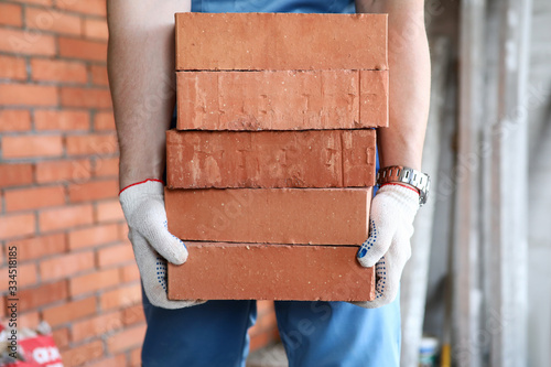 Gloved builder manually carries brick construction