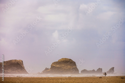 Surfer hiking along a shoreline of sand and rocks on Ecola State Park Beach of Oregon USA