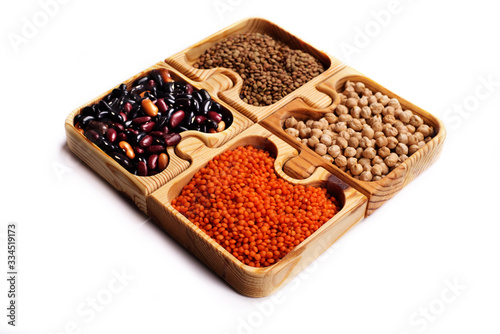 Legumes in brown wooden puzzle form on a white background. Green and red lentils, beans and chickpeas