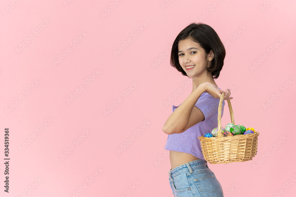 Cheerful Asian pretty girl holding up a wooden basket with colorful Easter eggs inside. Colourful Easter eggs in the festival celebrating. Cute girl's portrait in Easter egg festival concept. Cheerful Asian pretty girl holding up a wooden basket with colorful Easter eggs inside. Colourful Easter eggs in the festival celebrating. Cute girl's portrait in Easter egg festival concept.