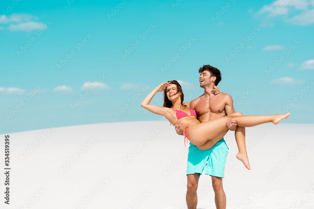 young man holding beautiful sexy girlfriend in arms on sandy beach