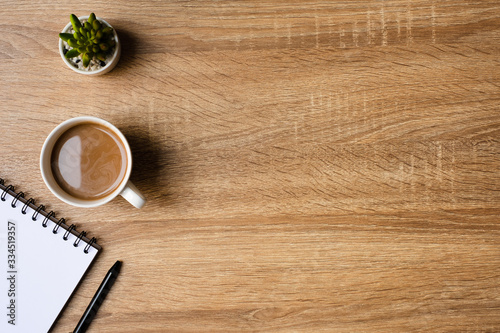 desk office with blank notepad, coffee cup and pen on wood table. Flat lay top view copy spce.