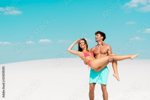 young man holding beautiful sexy girlfriend in arms on sandy beach