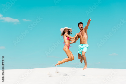 smiling young couple jumping together on sandy beach