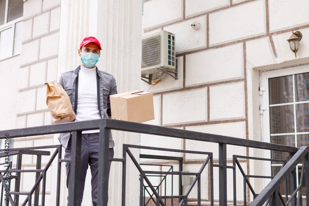 Courier in protective mask and medical gloves delivers takeaway food. Delivery service under quarantine, disease outbreak, coronavirus covid-19 pandemic conditions. Courier in protective mask and medical gloves delivers takeaway food. Delivery service under quarantine, disease outbreak, coronavirus covid-19 pandemic conditions.