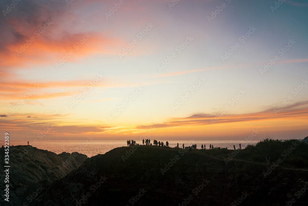 A crowd of people admire the sunset on a cliff on the Pacific Ocean