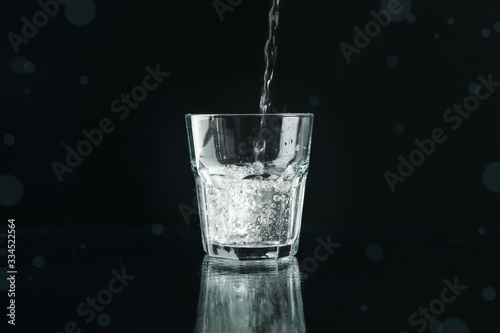 Pouring purified fresh water in glass on mirror background