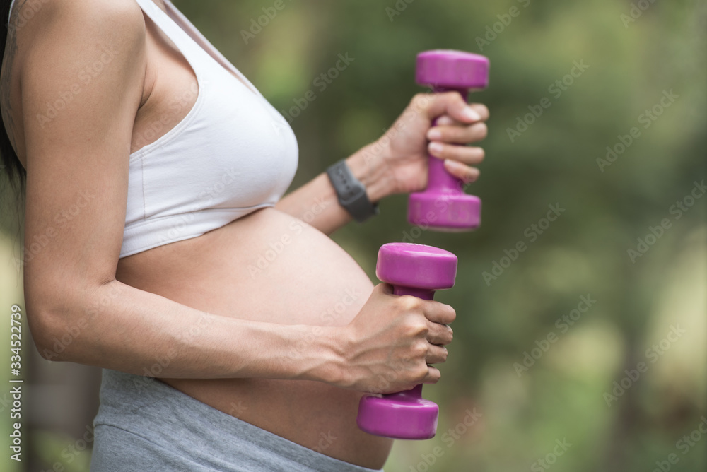 cropped image of a pregnant woman exercising with dumbbells. active and sportive pregnancy, healthy motherhood concept. fitness and healthy lifestyle during pregnancy. green nature bokeh background. cropped image of a pregnant woman exercising with dumbbells. active and sportive pregnancy, healthy motherhood concept. fitness and healthy lifestyle during pregnancy. green nature bokeh background.