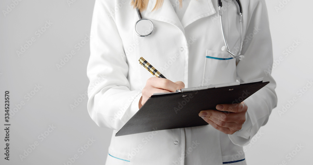 Midsection of female doctor holding clipboard and pen filling out medical document, isolated on white Midsection of female doctor holding clipboard and pen filling out medical document, isolated on white