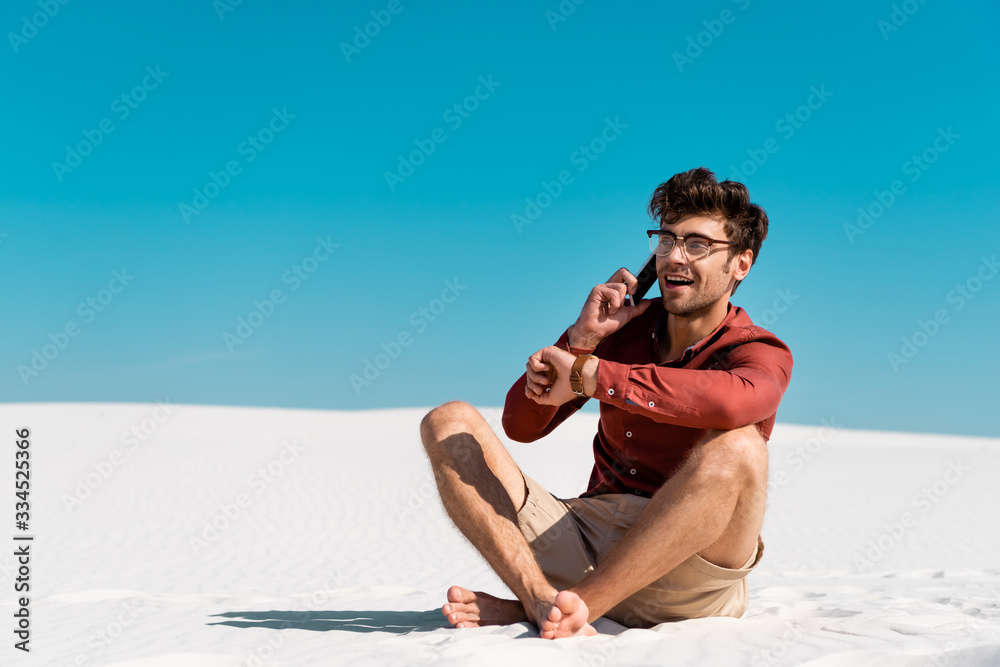 happy man on sandy beach talking on smartphone against clear blue sky happy man on sandy beach talking on smartphone against clear blue sky