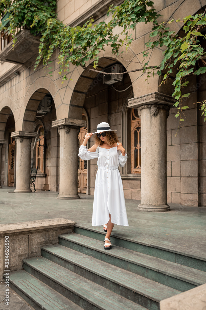 Fashion girl female looking the old city. Girl in Europe. Travel concept. Beautiful girl in white dress and hat. Fashion model on the street background. Lifestyle, travel, vacation, tourism
