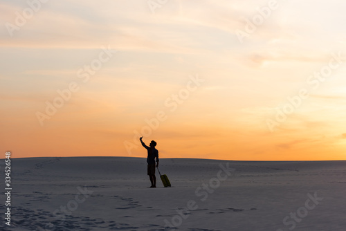 silhouette of man walking on beach with travel bag and smartphone at sunset