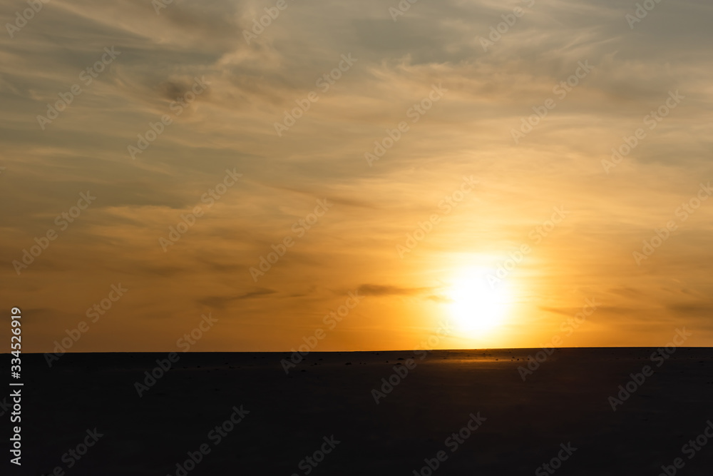 dark sandy beach against bright sun during sunset